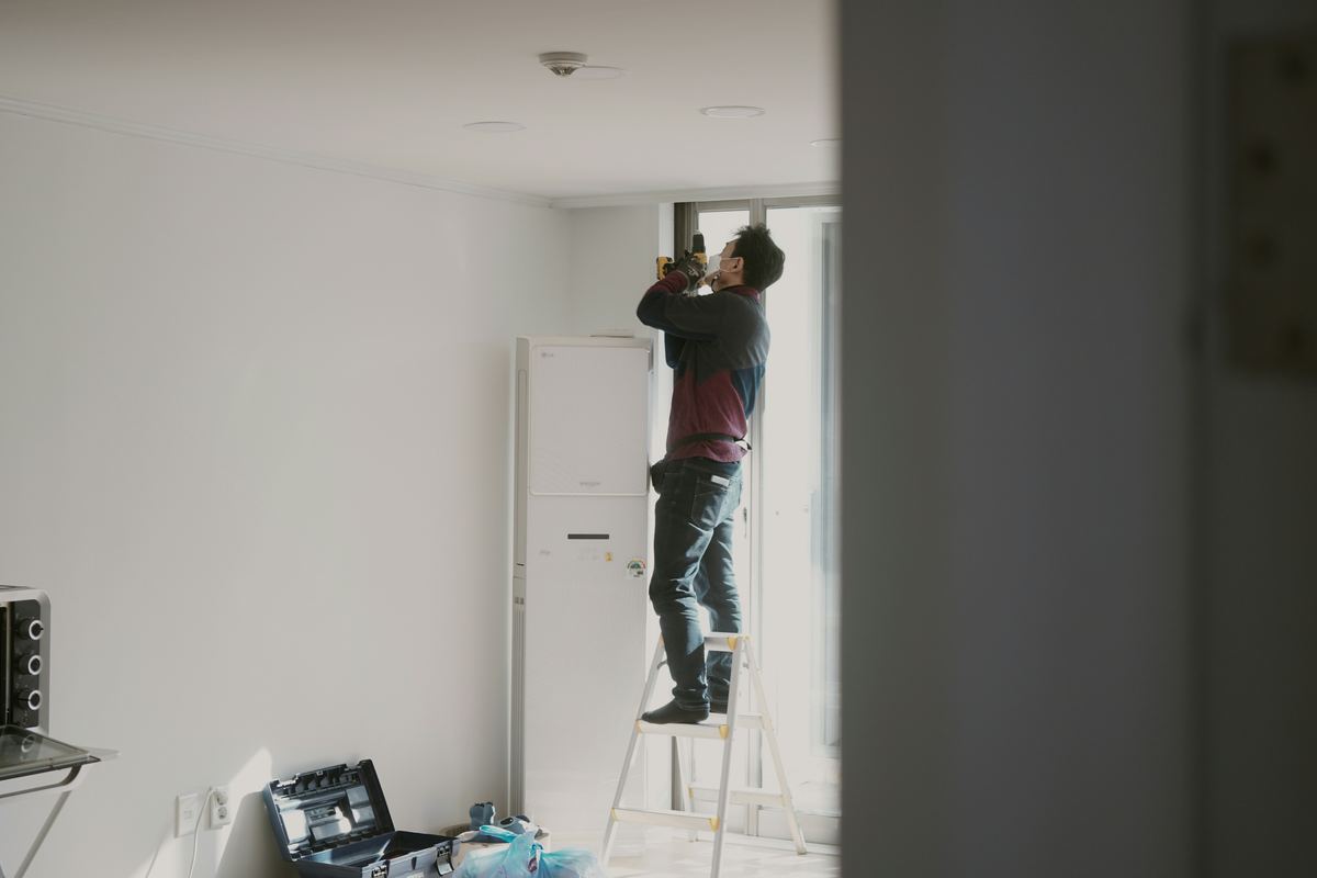 Vakman op een ladder in een witte kamer, gereedschapskoffer op de vloer